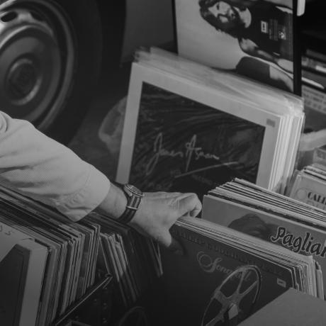A Black and white photo of a man picking a stack of records.