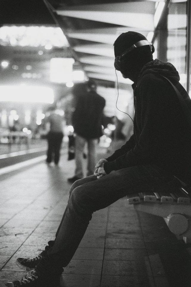 A black and white photo of a man sitting on a bench at night.